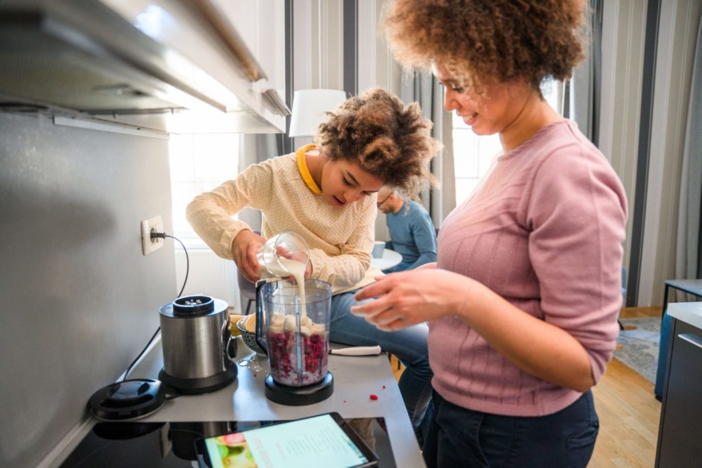 La mère et la fille préparent un smoothie pour le bol à smoothie dans un mixeur. Elles mettent des framboises et du lait dans un mixeur. Elles utilisent une tablette numérique et lisent la recette.